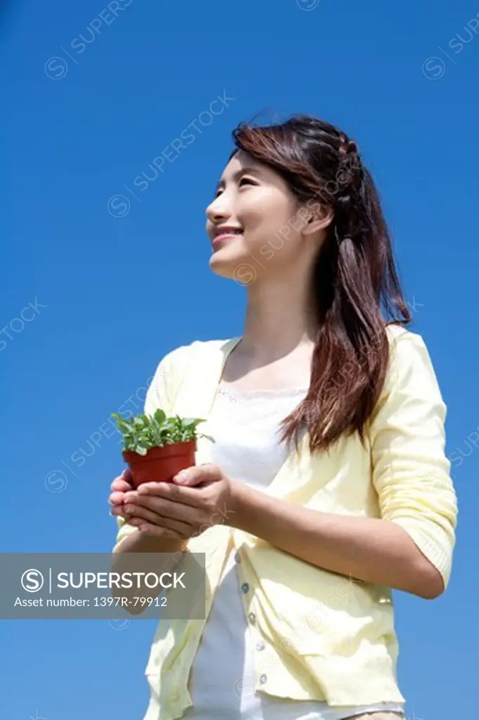 Young woman holding potted plant and looking up with smile
