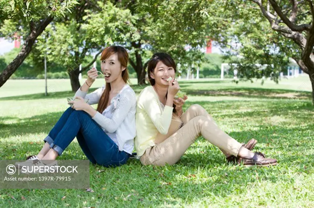 Young women sitting on the lawn and eating with smile