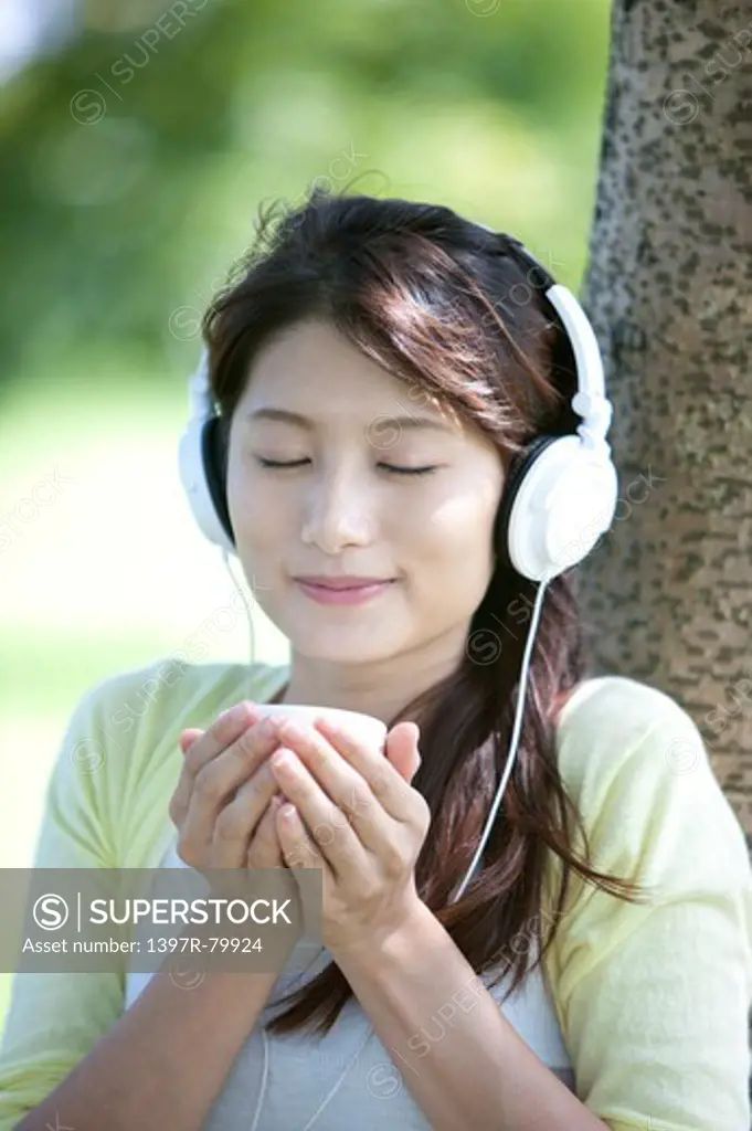 Young woman holding a cup and listening music with eyes closed