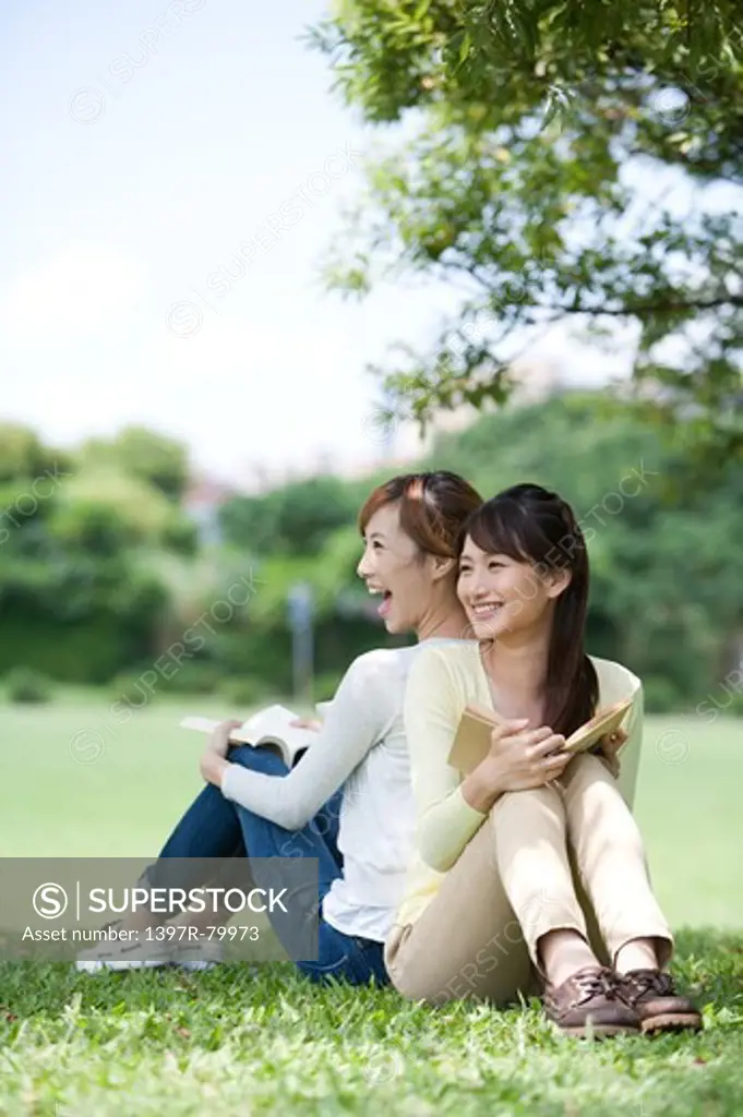 Young women sitting on the lawn with back to back and smiling happily