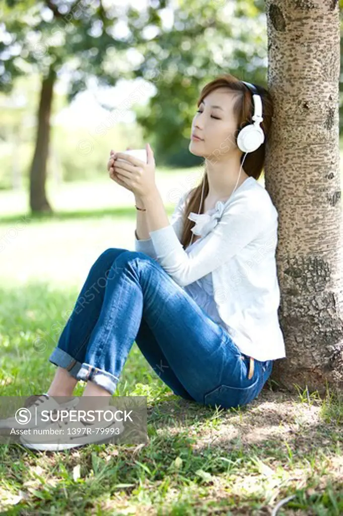 Young woman sitting on the lawn and holding cup with eyes closed