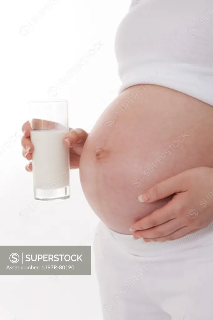 Pregnant woman holding a glass of milk and hand on abdomen