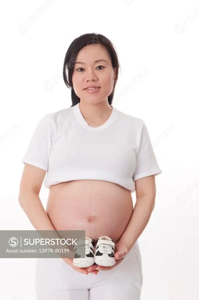 Pregnant woman holding a pair of baby booties and smiling at the camera