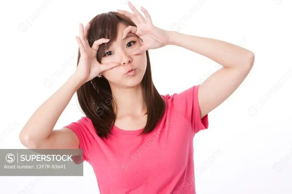 Young woman looking through fingers, making 'ok' sign