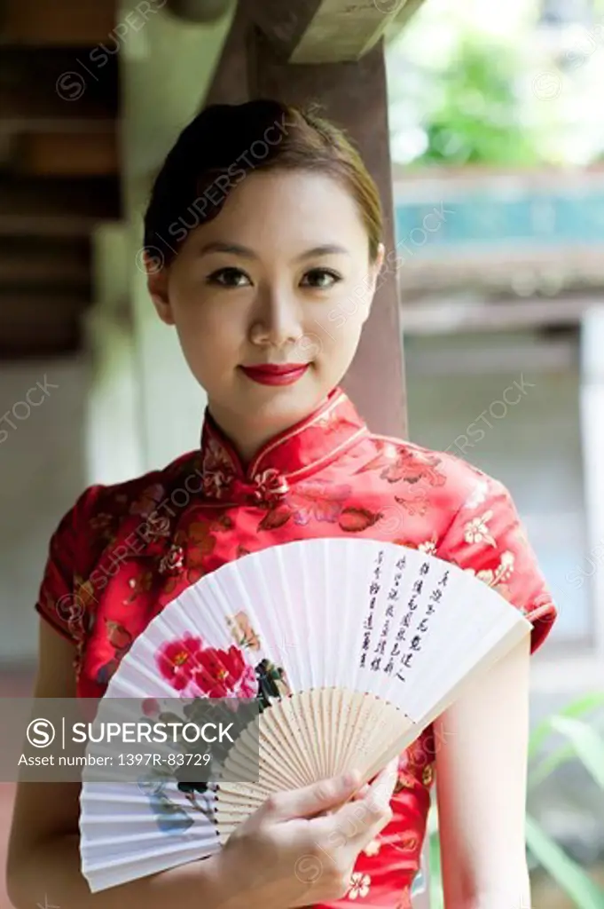 Young woman wearing cheongsam and holding folding fan with smile