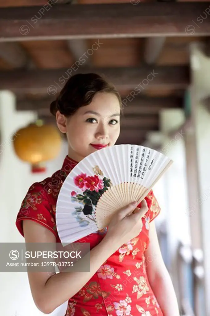 Young woman wearing cheongsam and holding folding fan with smile