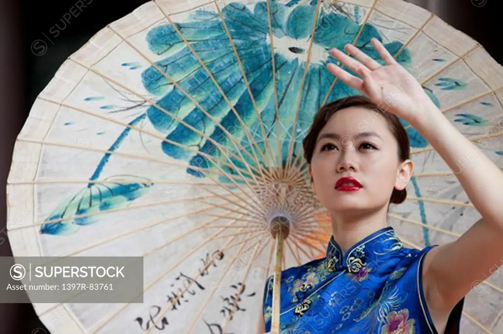 Young woman with cheongsam and looking up with paper umbrella