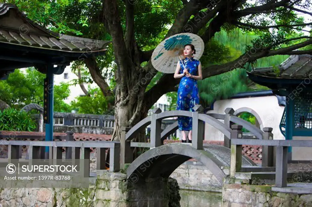 Young woman with cheongsam holding paper umbrella and looking away
