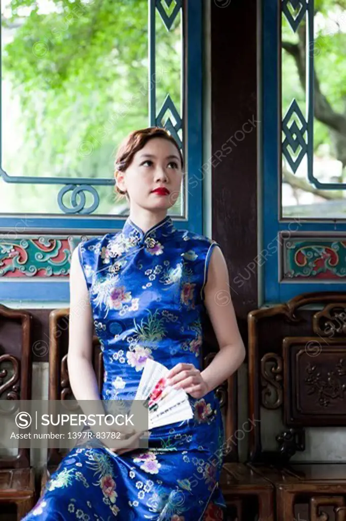 Young woman with cheongsam holding folding fan and looking up