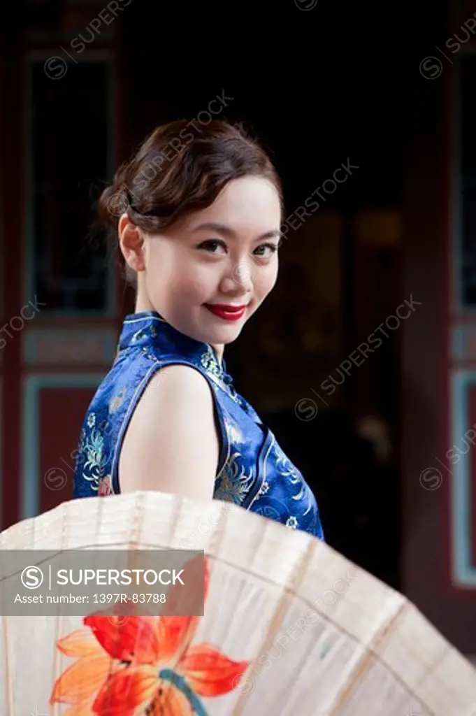 Young woman with cheongsam smiling at the camera with paper umbrella