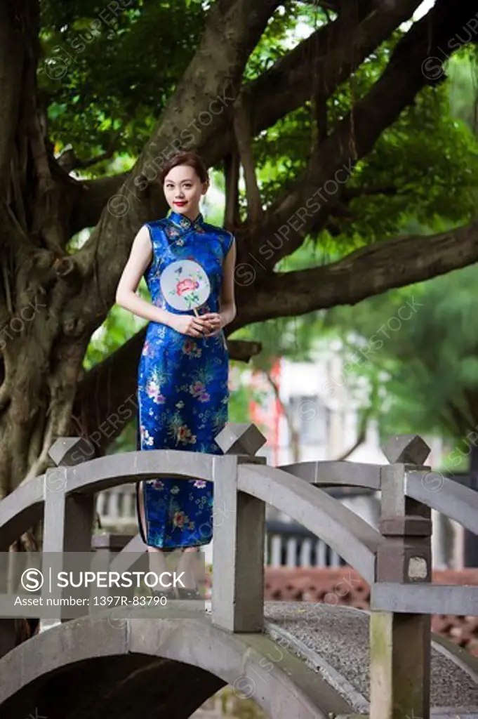 Young woman with cheongsam holding fan and standing with smile