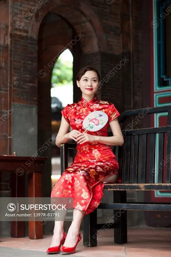 Young woman with cheongsam sitting and holding a fan with smile
