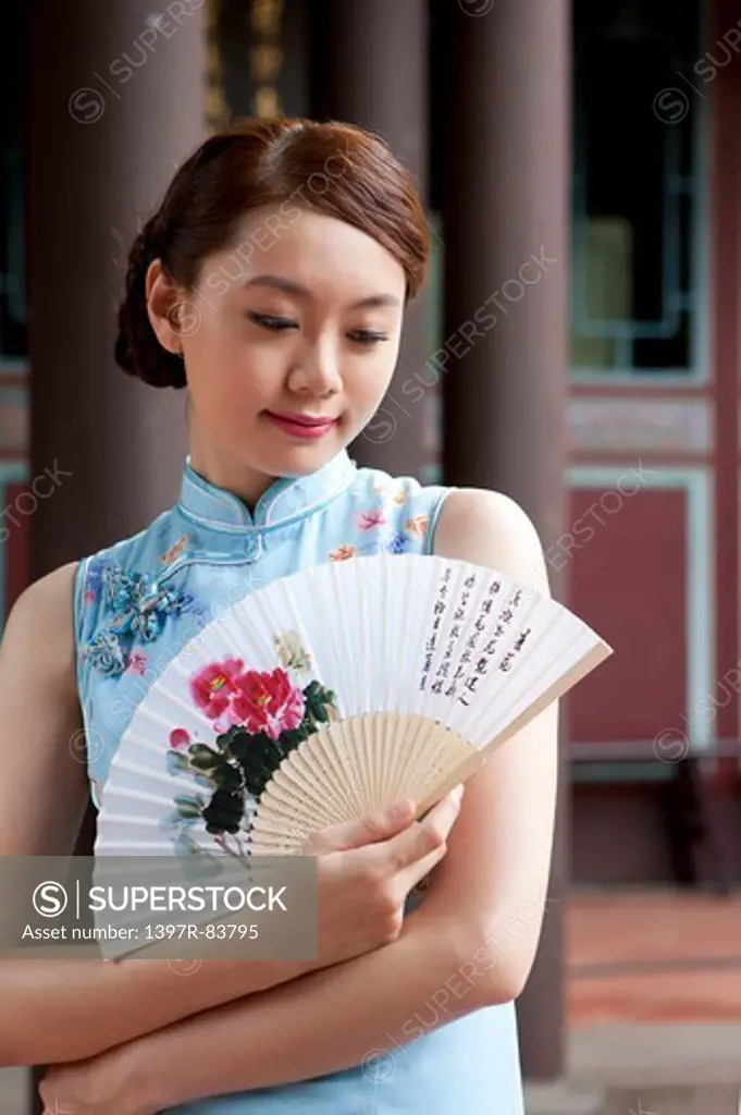 Young woman with cheongsam holding paper umbrella and looking down