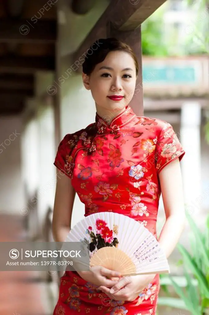 Young woman with cheongsam holding folding fan and looking at the camera