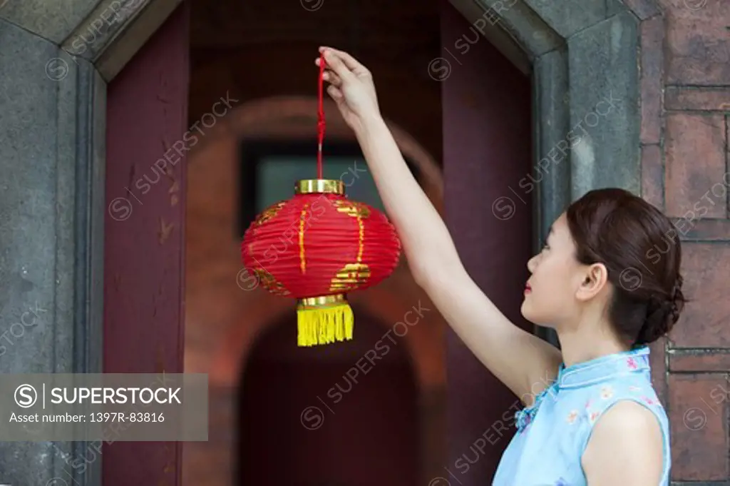 Young woman with cheongsam holding paper lantern and looking away