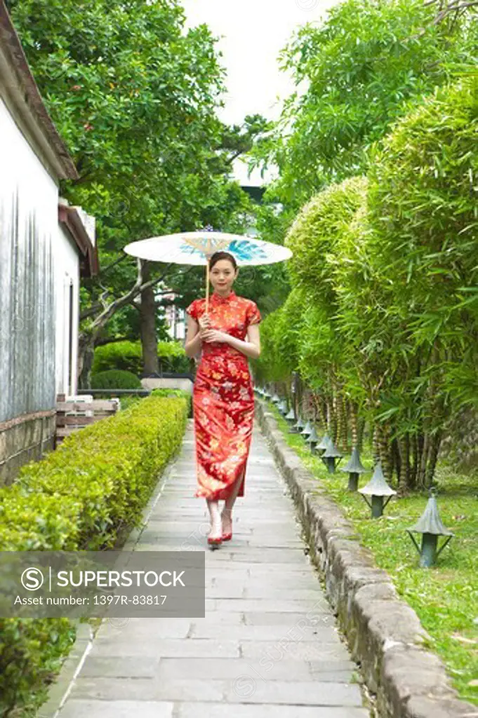 Young woman with cheongsam walking on the road and holding paper umbrella