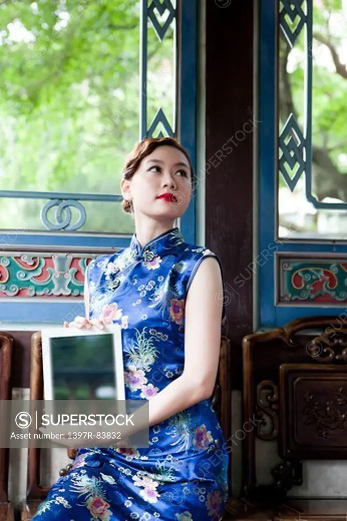 Young woman with cheongsam holding pad and looking up