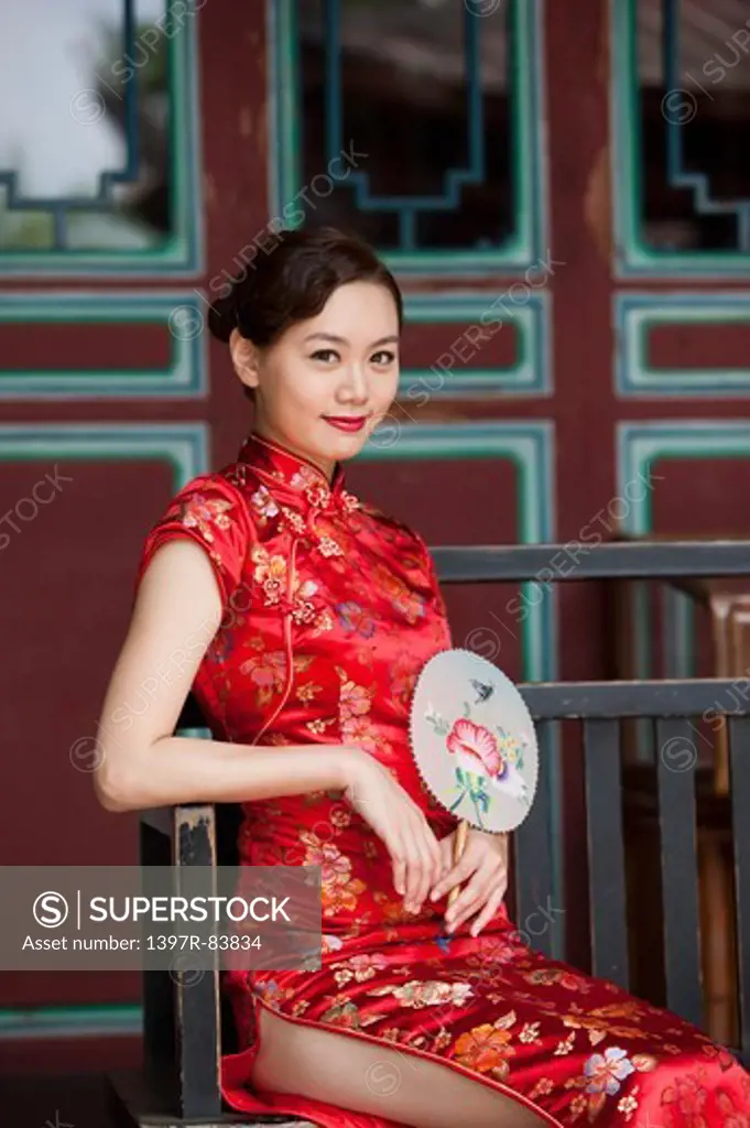Young woman wearing cheongsam and holding fan with smile