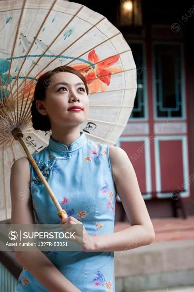 Young woman wearing cheongsam and holding paper umbrella with smile