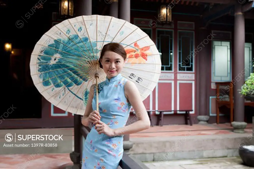 Young woman wearing cheongsam and holding paper umbrella with smile
