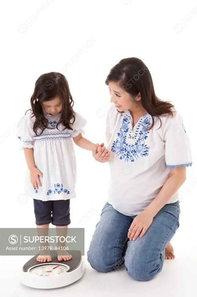 Daughter standing on weight scale and holding hands with mother