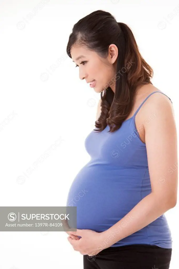Pregnant woman holding abdomen and looking down with smile
