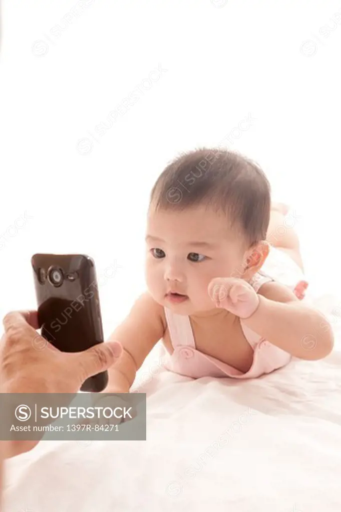 Baby girl crawling on sheet and looking at a mobile phone