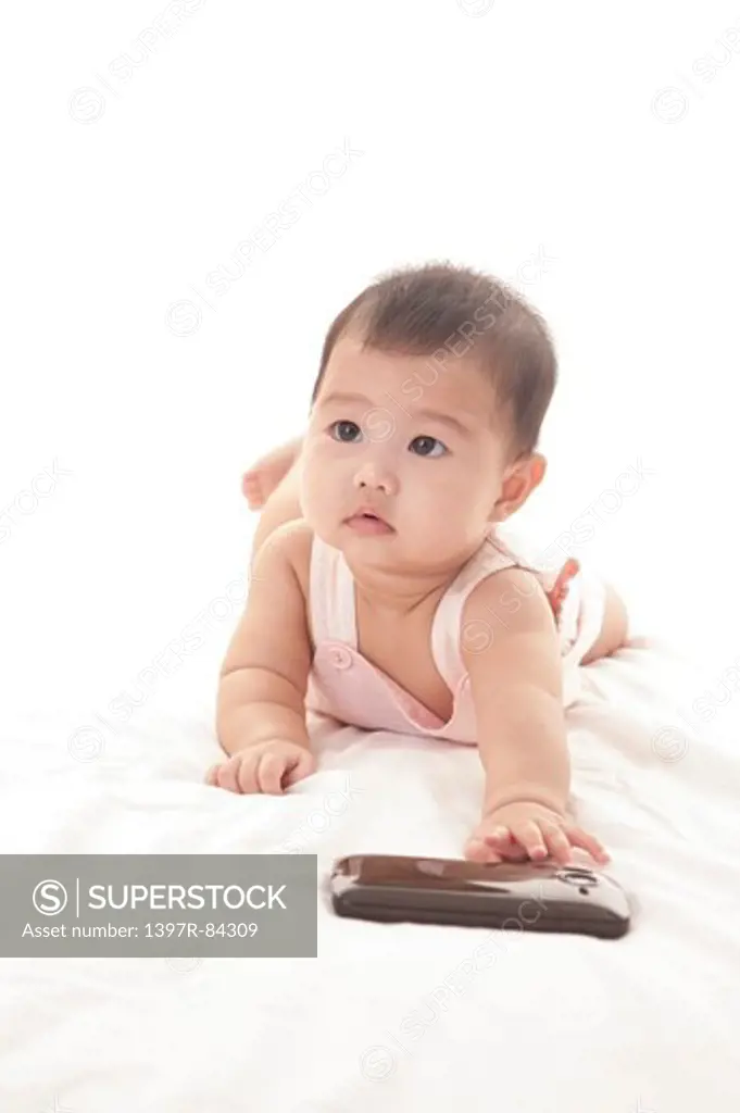 Baby girl crawling on sheet and touching a mobile phone
