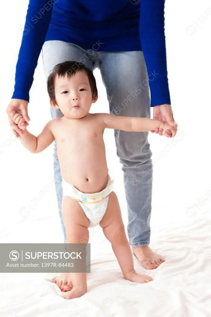 Baby girl walking on sheet with her mother holding her hands