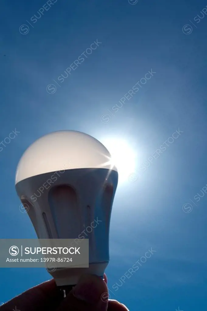 Human hand holding light bulb against sky