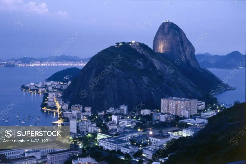 High angle view of buildings in a city lit up at dusk with a mountain in the background, Sugarloaf Mountain, Rio de Janeiro, Brazil