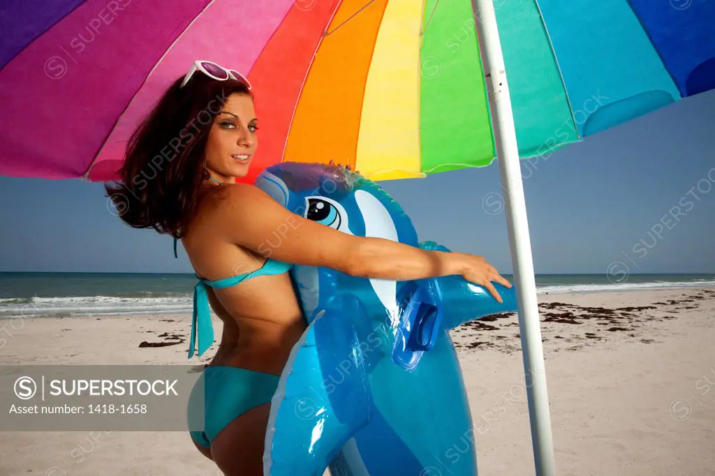 USA, Florida, Young woman with Inflatable whale standing under colorful umbrella on beach