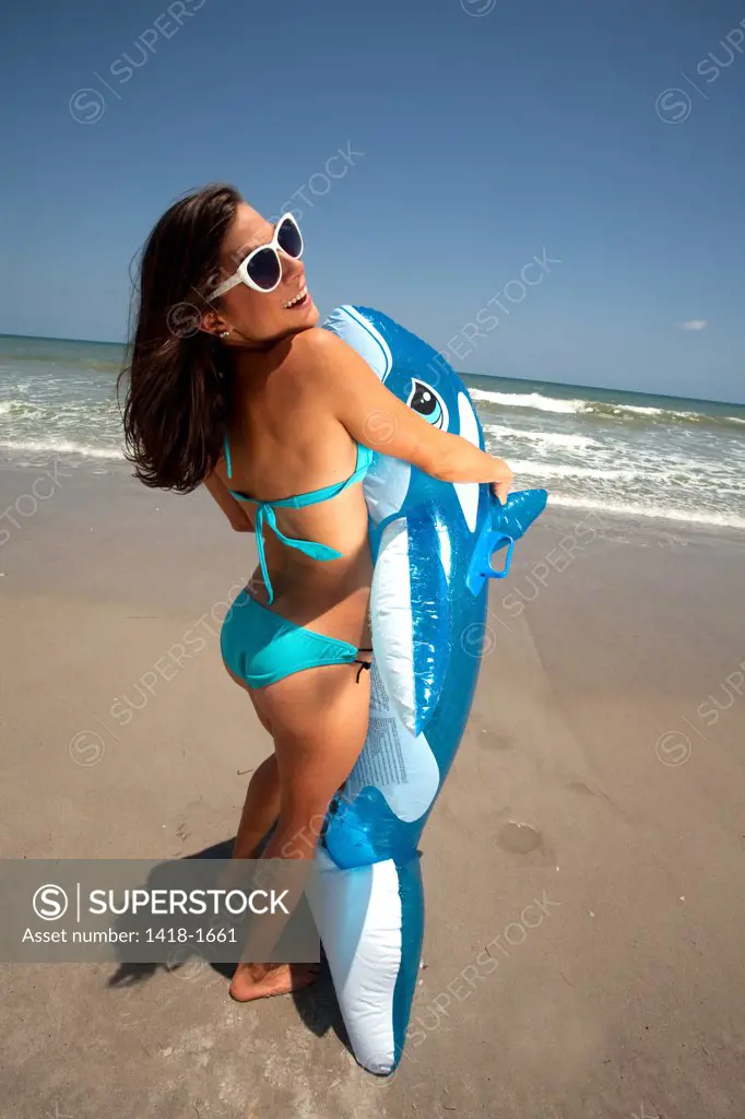 USA, Florida, Young woman playing with Inflatable whale on beach
