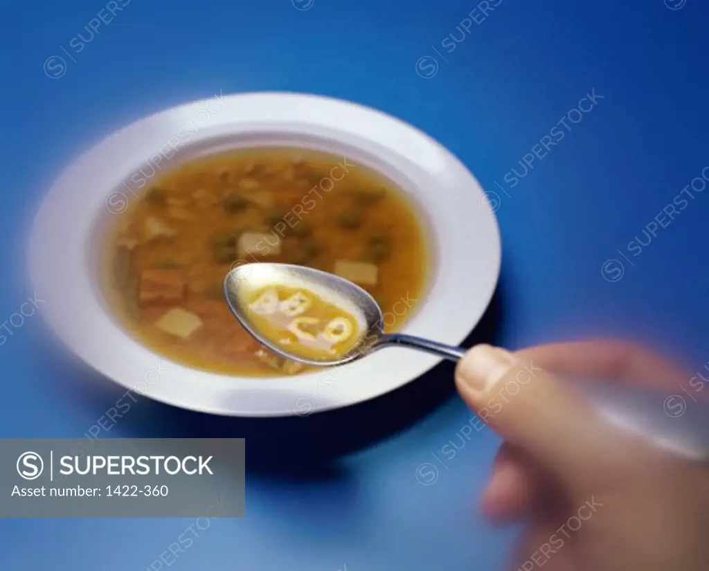 Close-up of a person's hand holding a spoon of alphabet soup