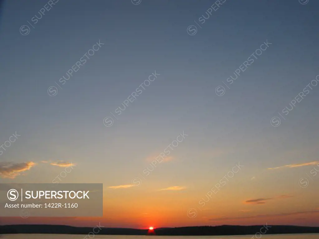 Sun setting on horizon of land with clear sky at dusk