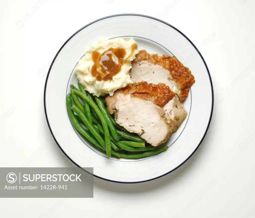 Two slices of turkey, green beans and mashed potatoes with brown gravy on plate