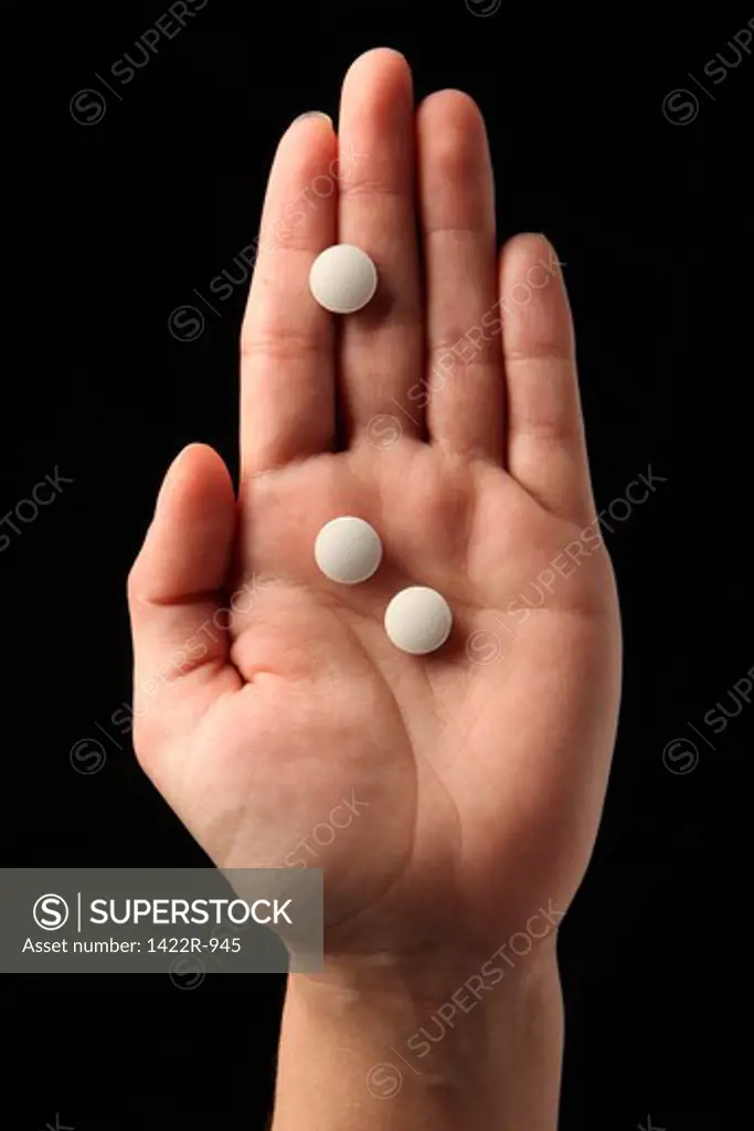 Three white pills in the palm of a person