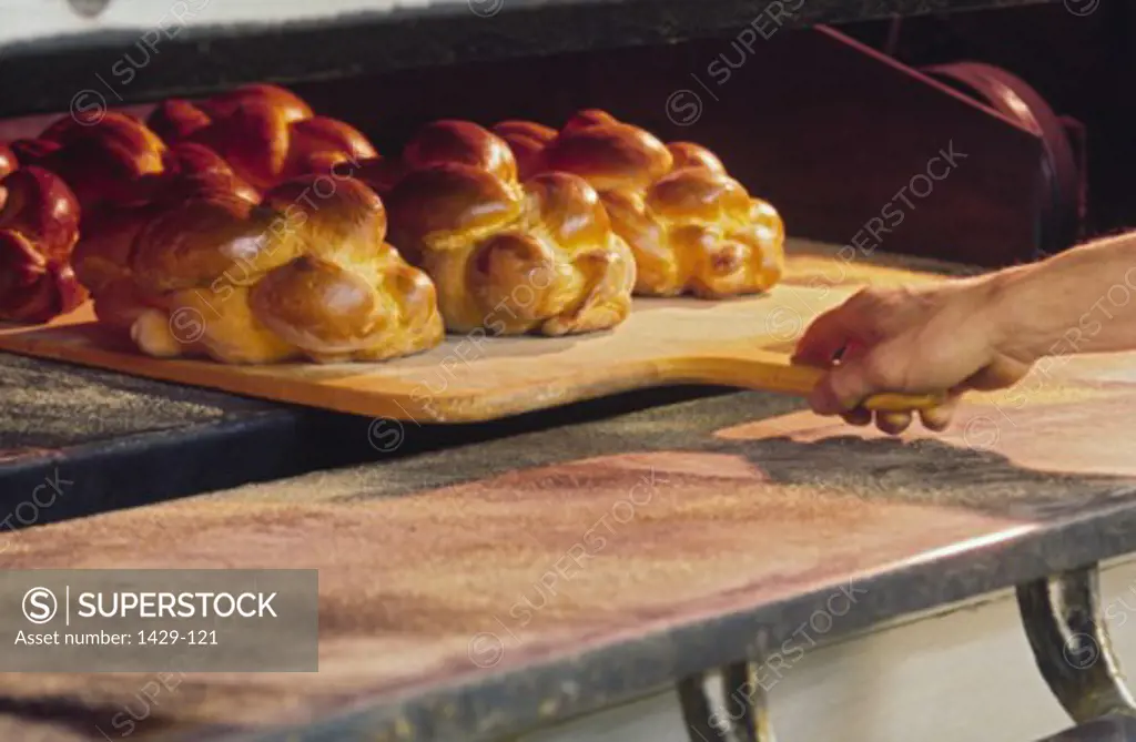 Close-up of a person's hand taking out baked challahs from an oven