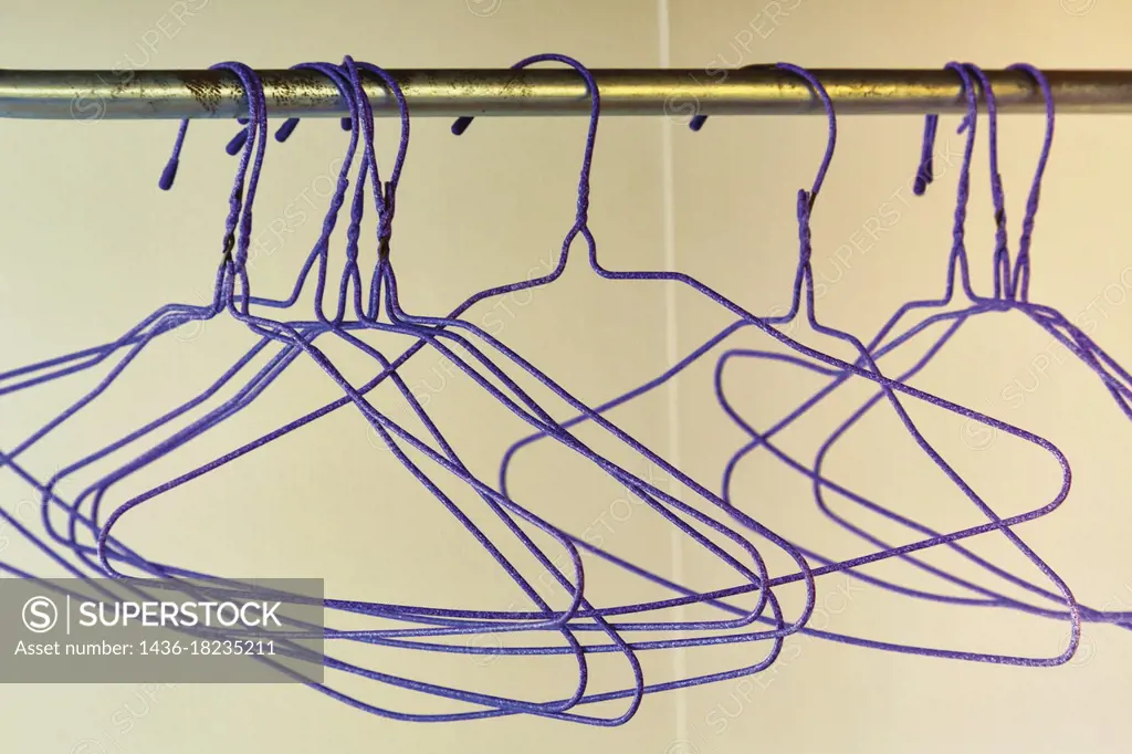 Group of empty purple wire coat hangers hanging on rail.