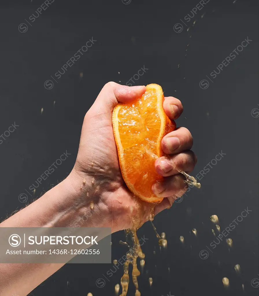 Male hand squeezing juicy orange, dark background.