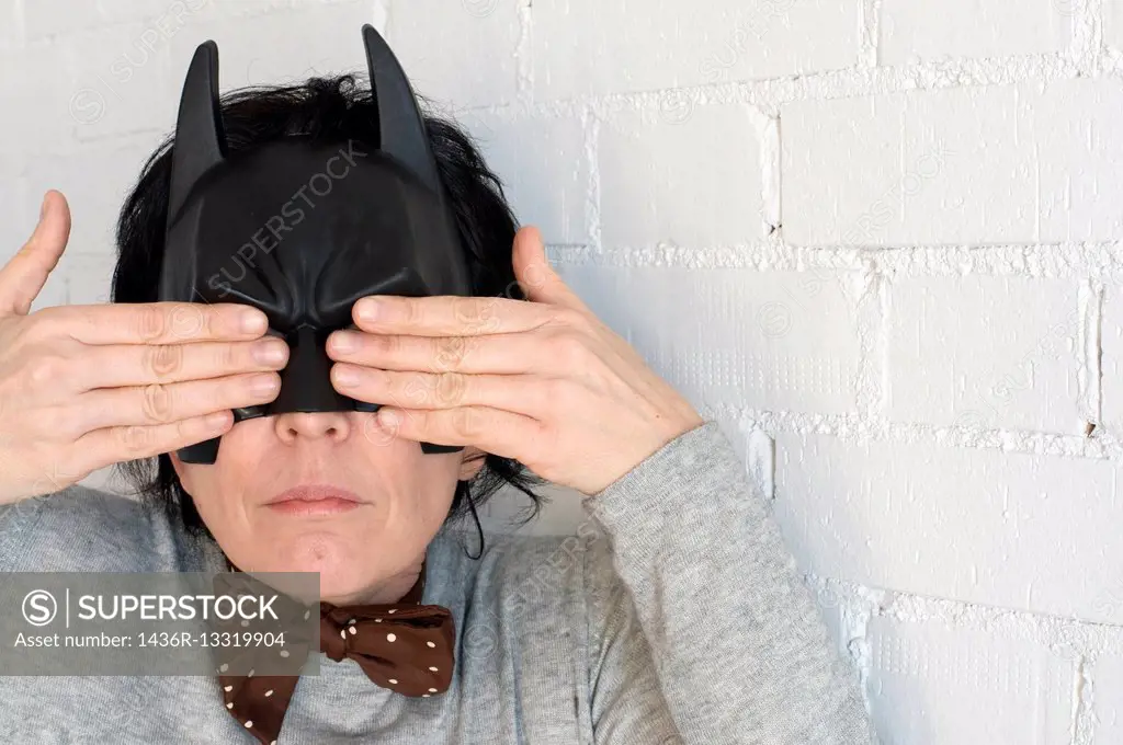 Young woman with a Batman mask and expression of a notty girl and with the hands covering her eyes.