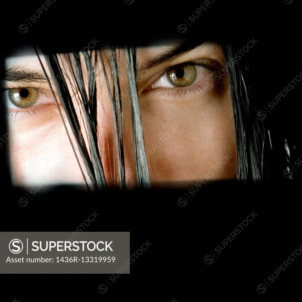 Green eyes of a young dark-haired woman staring at the camera through a slot.