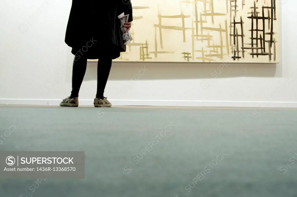Back view of the legs of a woman looking at a painting in a museum.