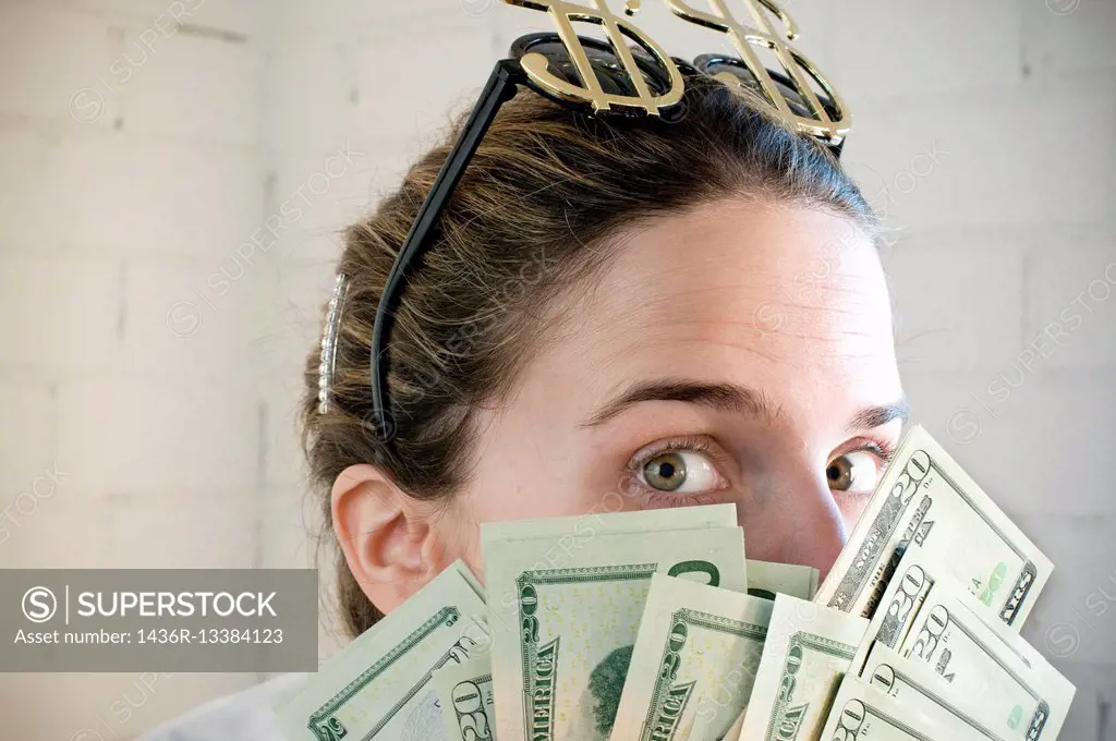 Young woman with sunglasses with a symbol of the dollar and hidden behind a lots of dollars in hands.