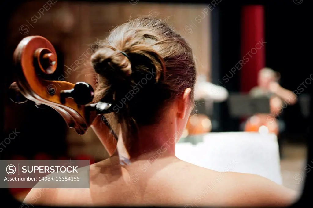 Close up of a rear view of a musician playing a cello on a stage in a theater.