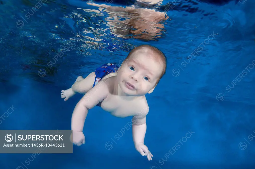 2 months infant boy learning to swim underwater in waterbaby class in the pool.