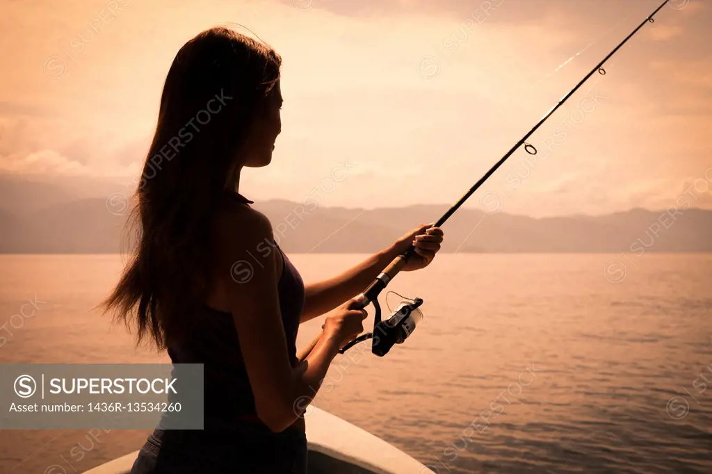 Young woman holding fishing pole at sunset. Banderas Bay - Pacific Ocean, Puerto Vallarta, Mexico.