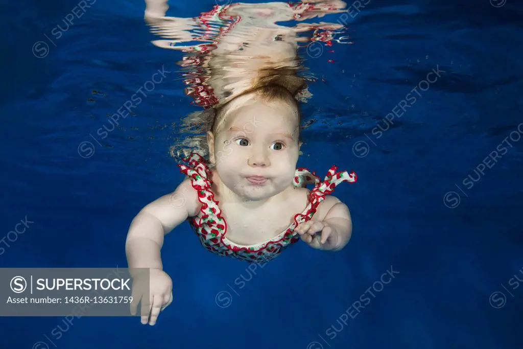 Little girl posing in a suit under water in the pool.