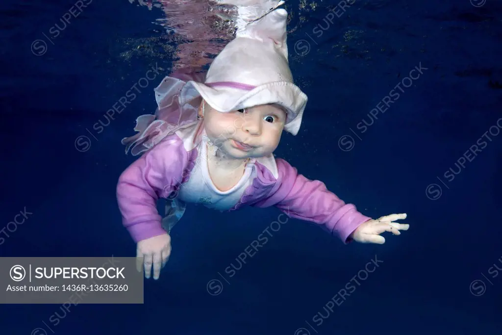 Little girl in a wizard costume posing under the water in the pool.