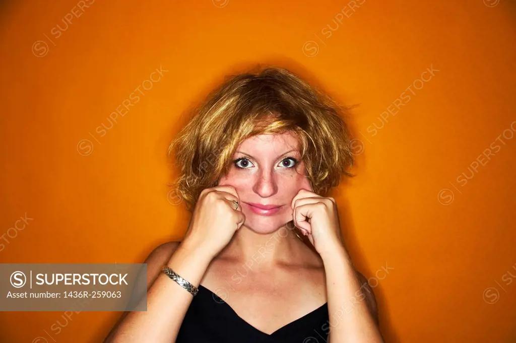 Young blond woman, with messy hair, pulling her cheeks